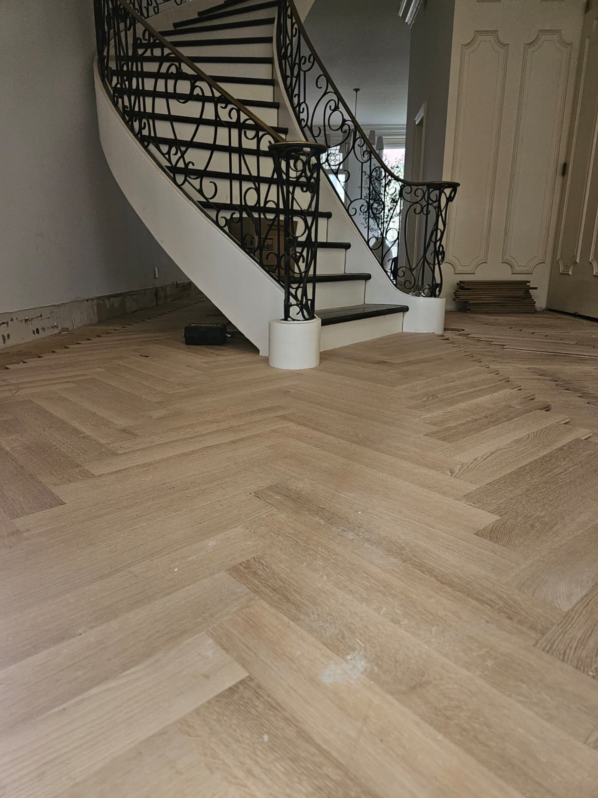 New white oak herringbone laid around the curved staircase of an Upper West Side brownstone