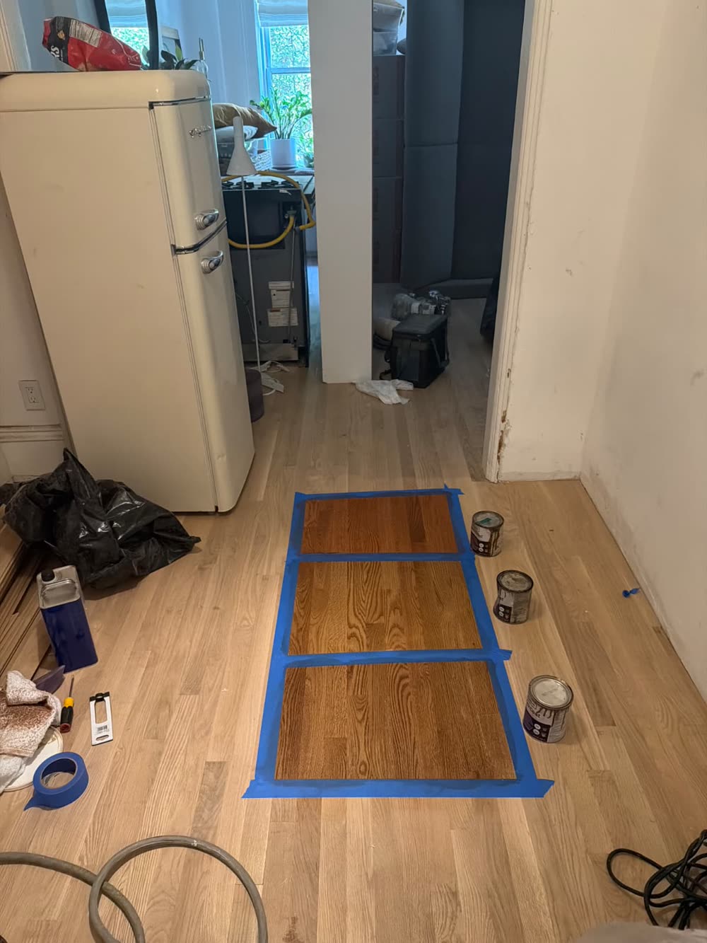 Three stain samples on a light oak floor, each taped off so they can be compared